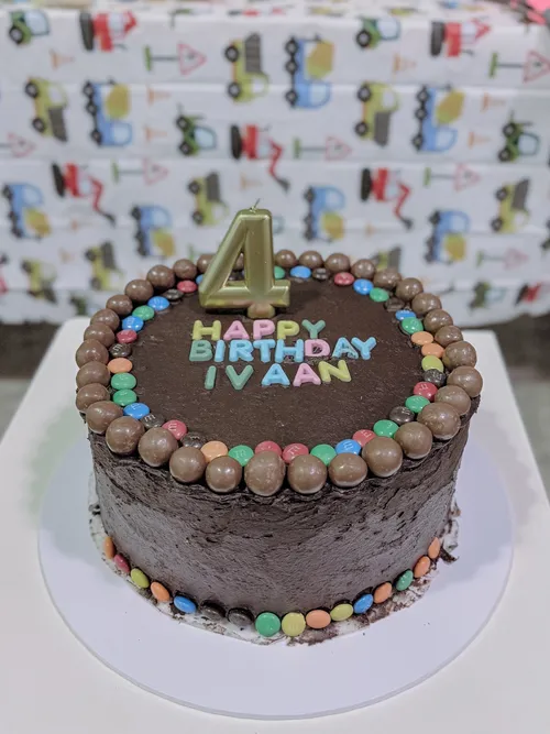 A chocolate birthday cake ringed with colourful chocolate beans and topped with a gold number four candle.