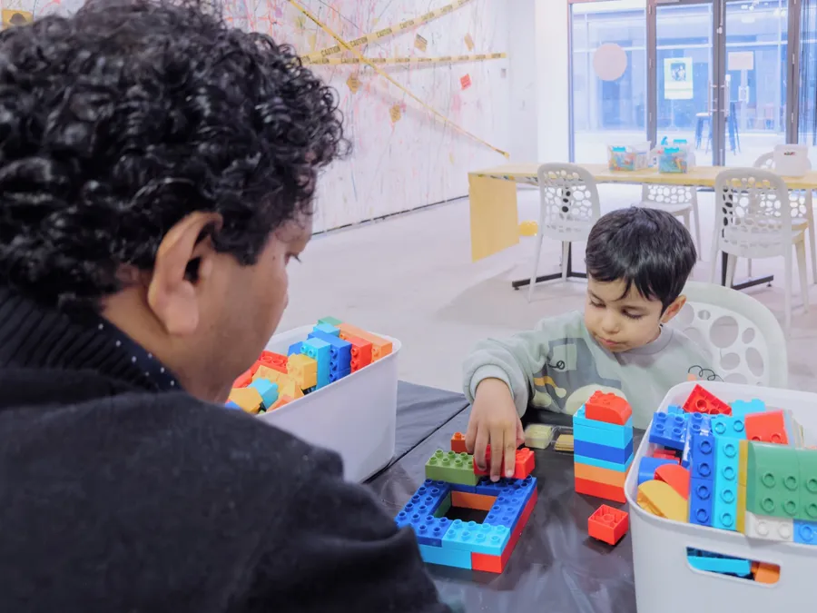 A father and his son build together with colourful blocks at a table.