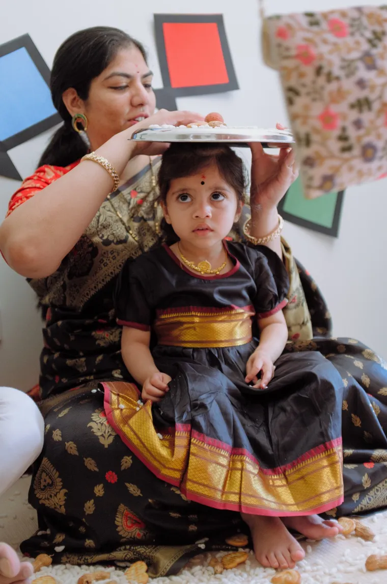 A mother holds a silver thali over her little girl during a first Makar Sankranti Bornhan ceremony.