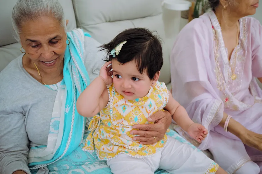 A grandmother sits with her baby granddaughter, who wears a yellow outfit, on the sofa.