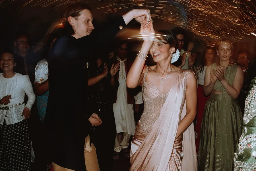 The groom twirls the bride on the dance floor as guests clap and cheer at the evening reception.