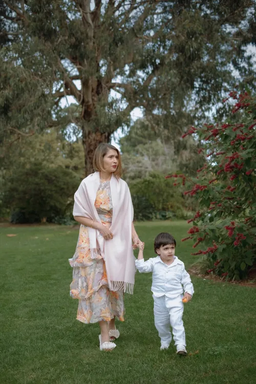 A mother walks hand in hand with her young son past a bush of red berries in the park.