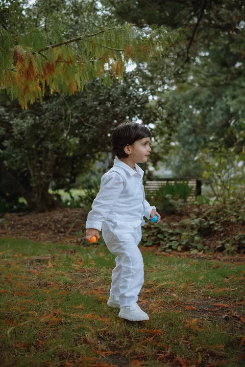A young boy in a white outfit walks through the park on a soft autumn afternoon.