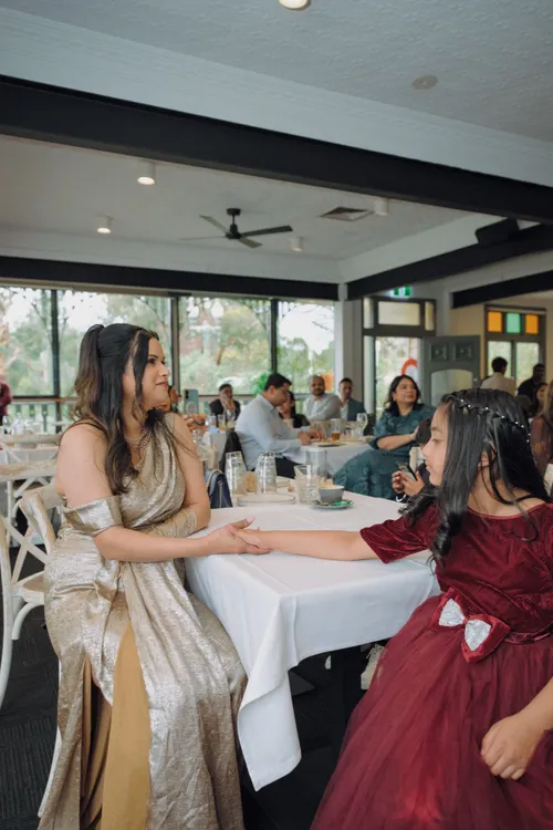 A mother reaches across a white tablecloth to hold her daughter's hand, smiling at her.