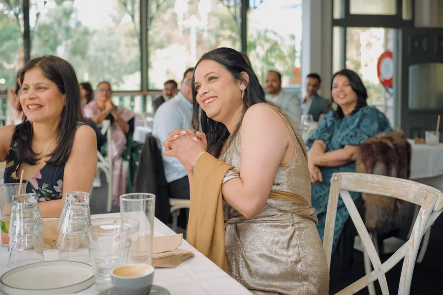 Two women at a long table laugh together, other guests seated behind them.