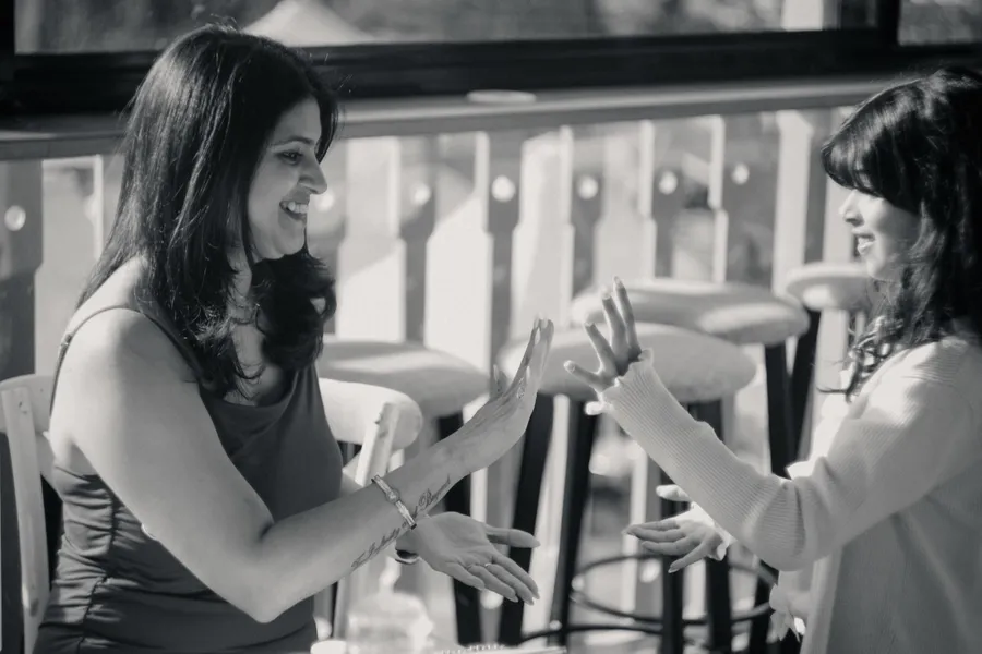 Black and white photo of two women laughing mid-conversation, hands raised between them.