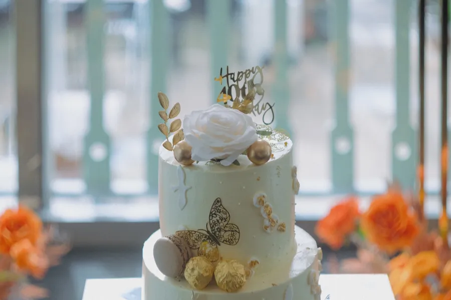 Close-up of the gold and white birthday cake and its Happy 40th topper, orange flowers soft behind.