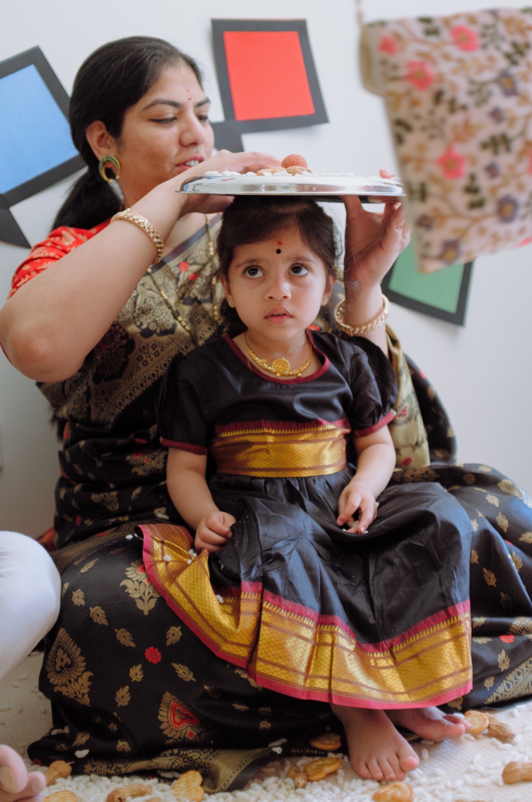 A mother holds a decorated thali over her daughter during the child’s first Makar Sankranti ceremony.